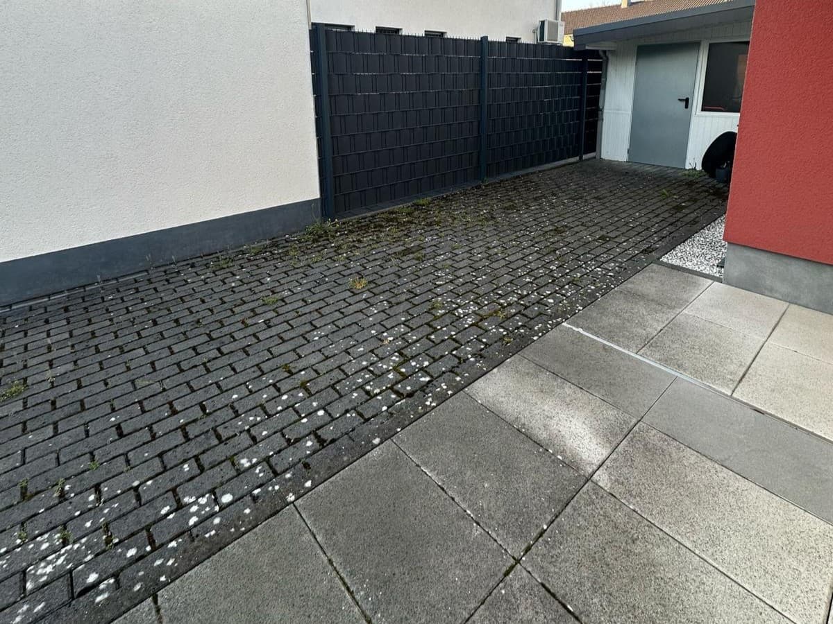 Anthrazitfarbenes Pflaster an Garage und Sichtschutzzaun: vorher mit Moos und Flechten, nachher gereinigt., vorher