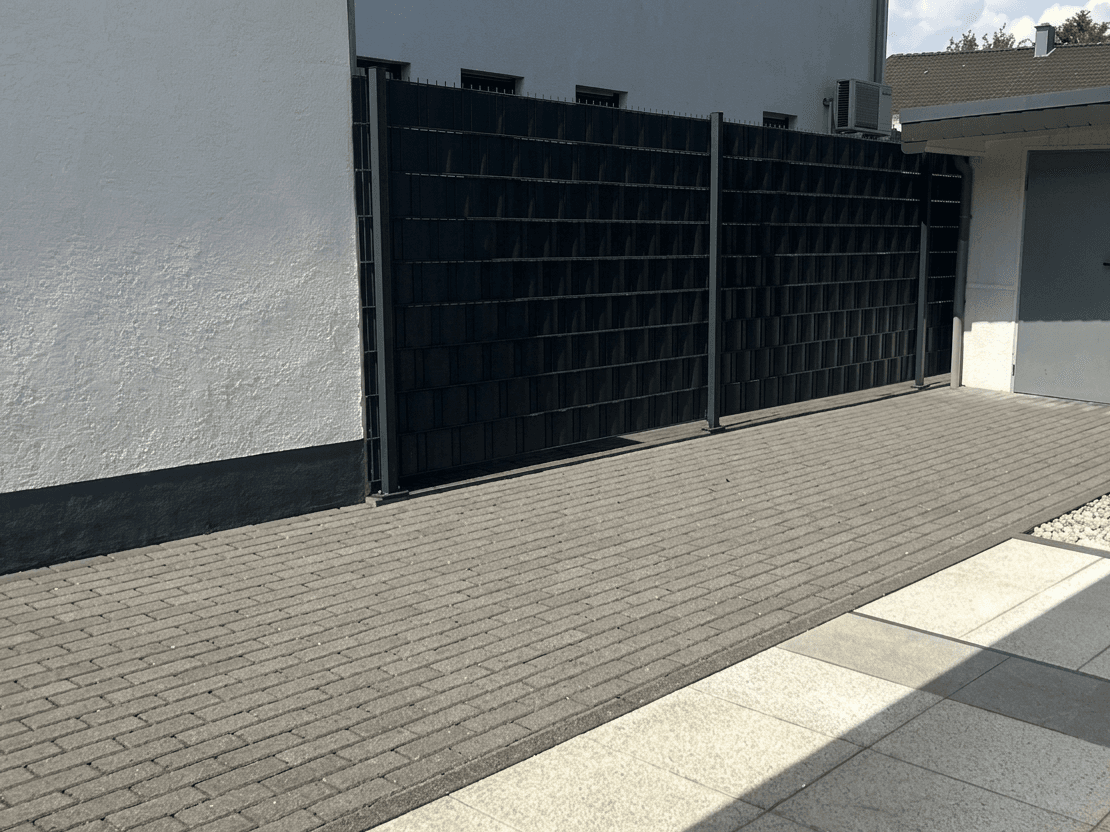 Anthrazitfarbenes Pflaster an Garage und Sichtschutzzaun: vorher mit Moos und Flechten, nachher gereinigt., nachher